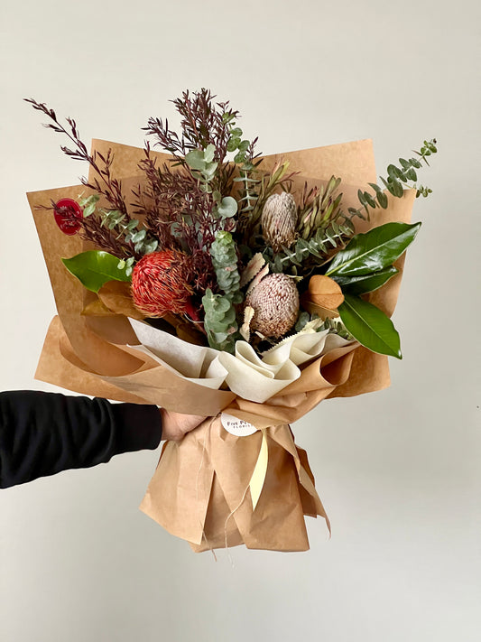 A small bouquet of native flowers with foliages wrapped in brown paper.