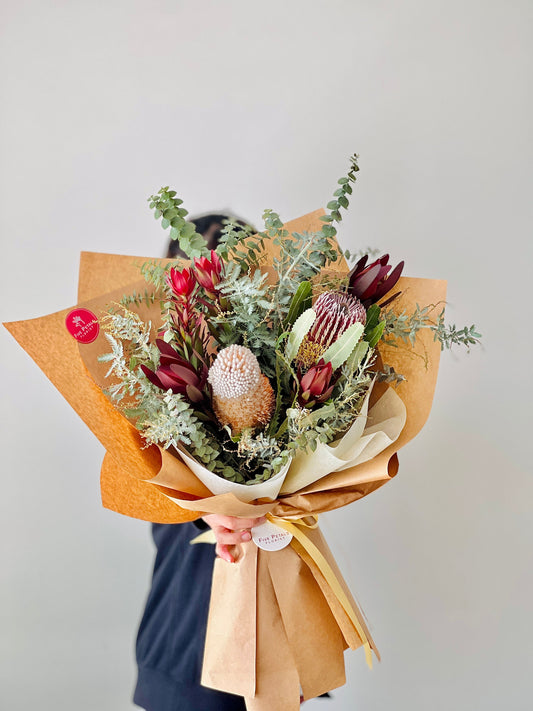 Native flowers and foliages in a bouquet wrapped in brown paper.