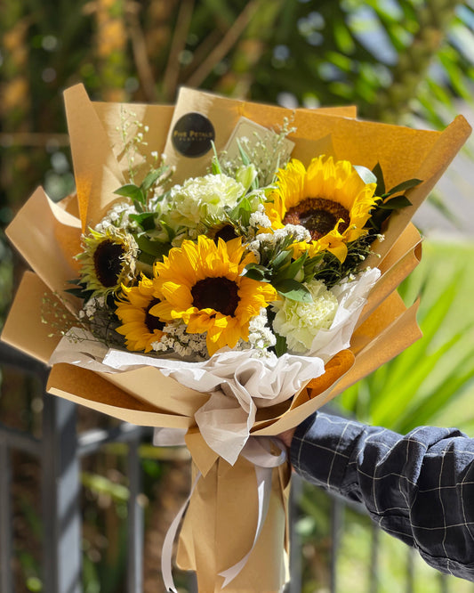A bouquet of Sunflowers, mix of carnations and foliages wrapped in a brown paper bouquet. 
